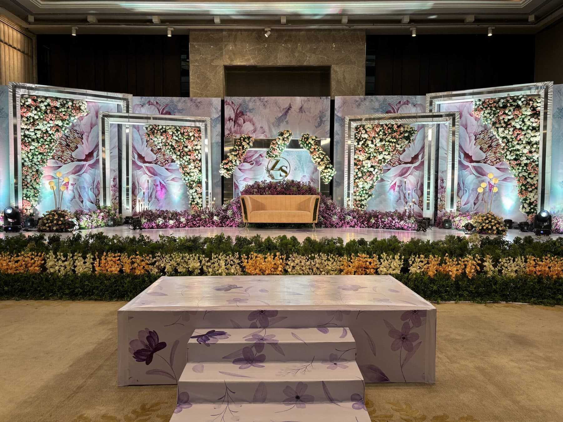 Floral wedding reception stage with layered backdrop panels and uplighting